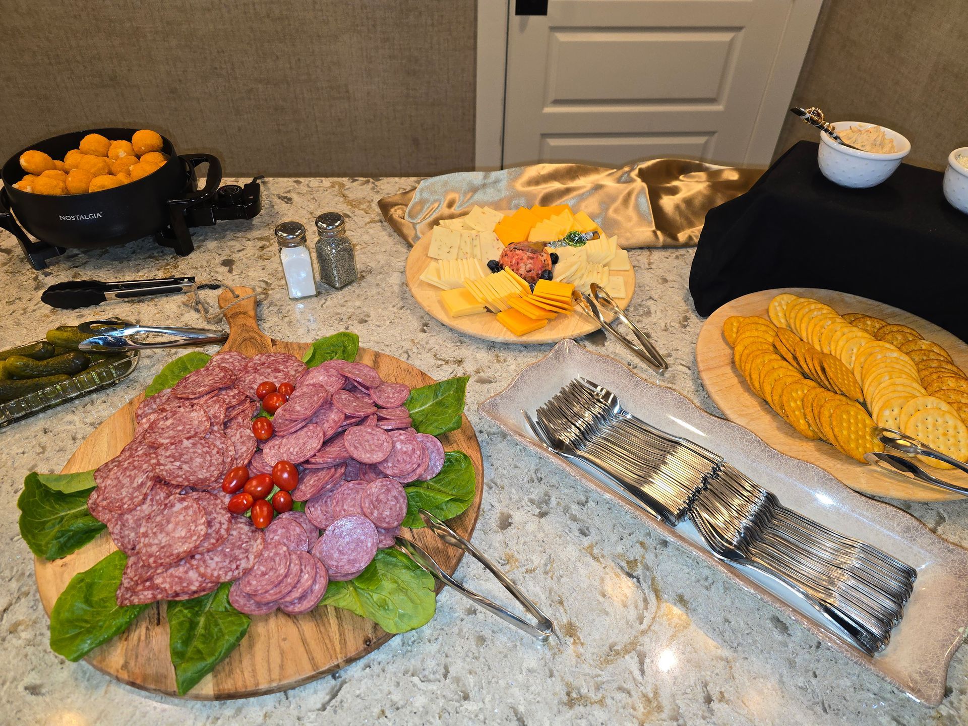 Buffet table with crackers, cheese, salami, fruit, and dips arranged on platters and trays