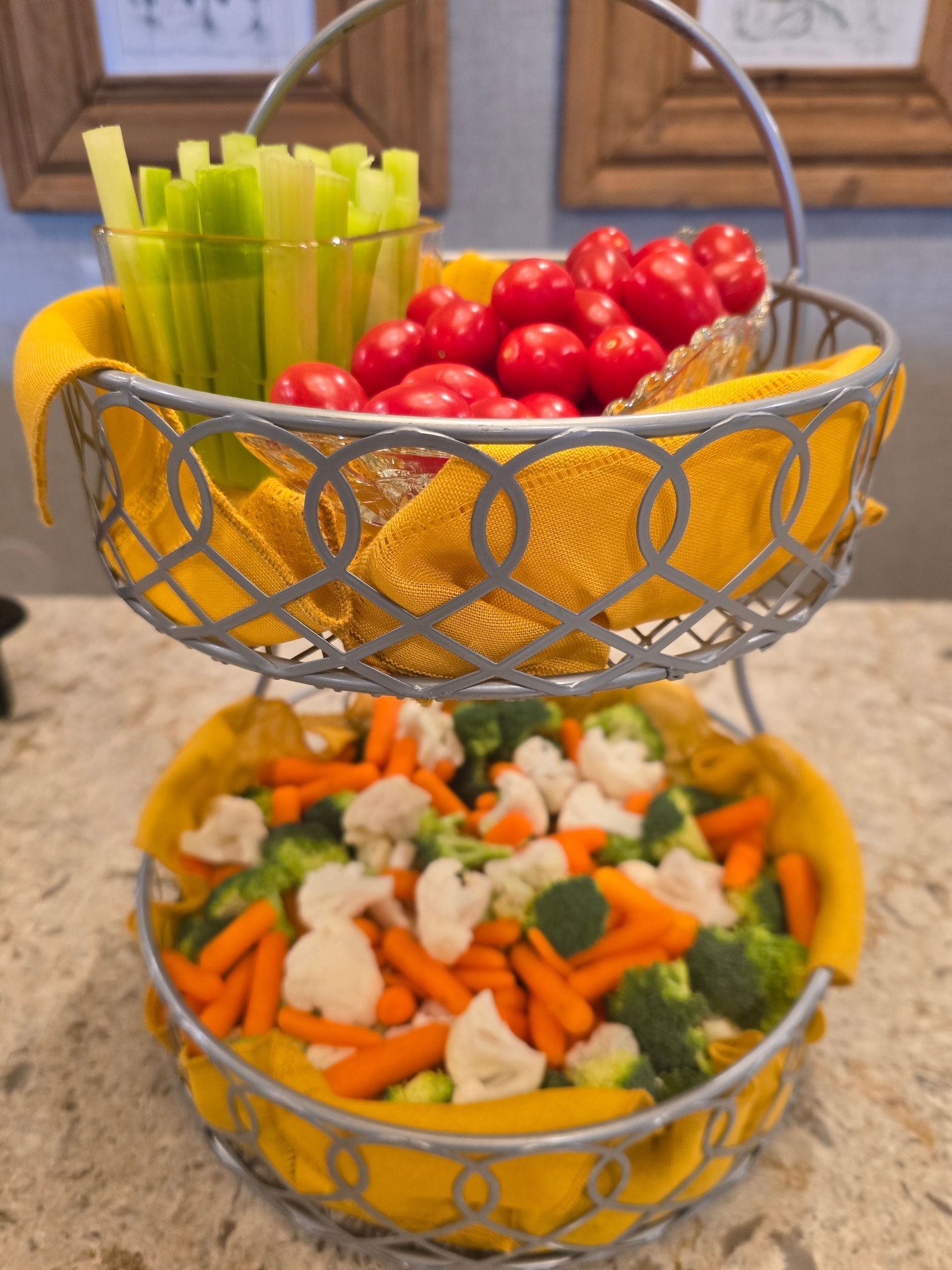 Two-tier gold wire basket with celery, cherry tomatoes, and mixed vegetables on a table