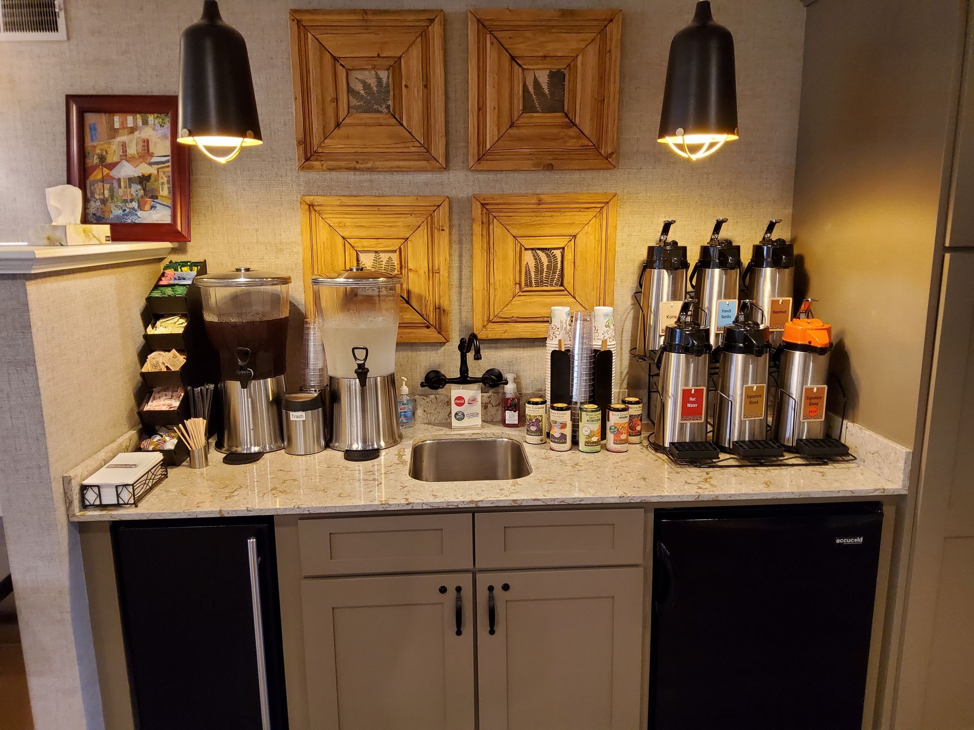Coffee bar with espresso machine, mugs, cups, and bottles on a granite counter beneath hanging lights