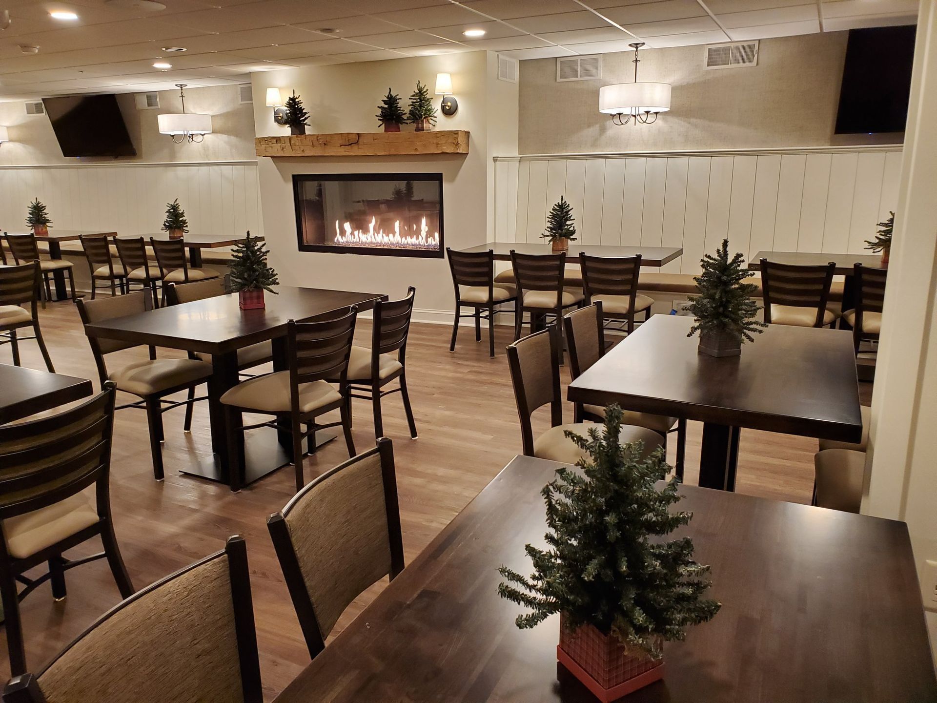 Empty dining room with wooden tables, chairs, and a lit fireplace in the back wall.