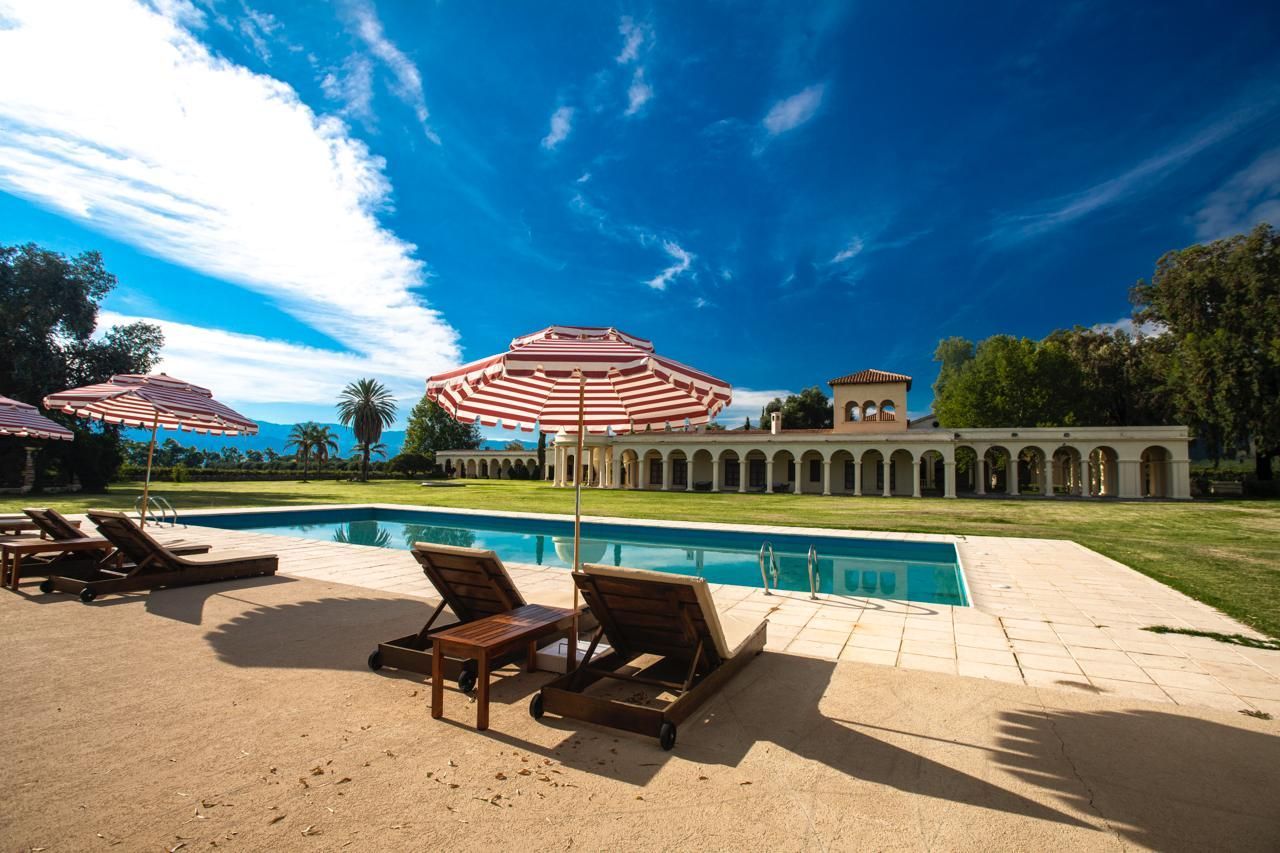 A swimming pool with lounge chairs and striped umbrellas in front of a large building on a sunny day.
