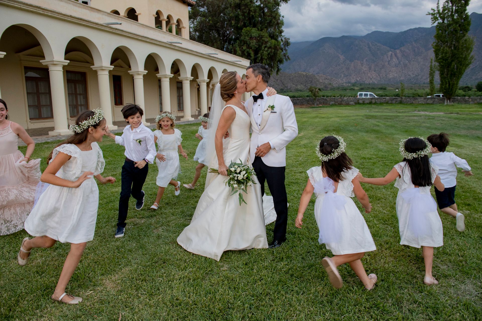 A bride and groom are kissing while surrounded by flower girls.