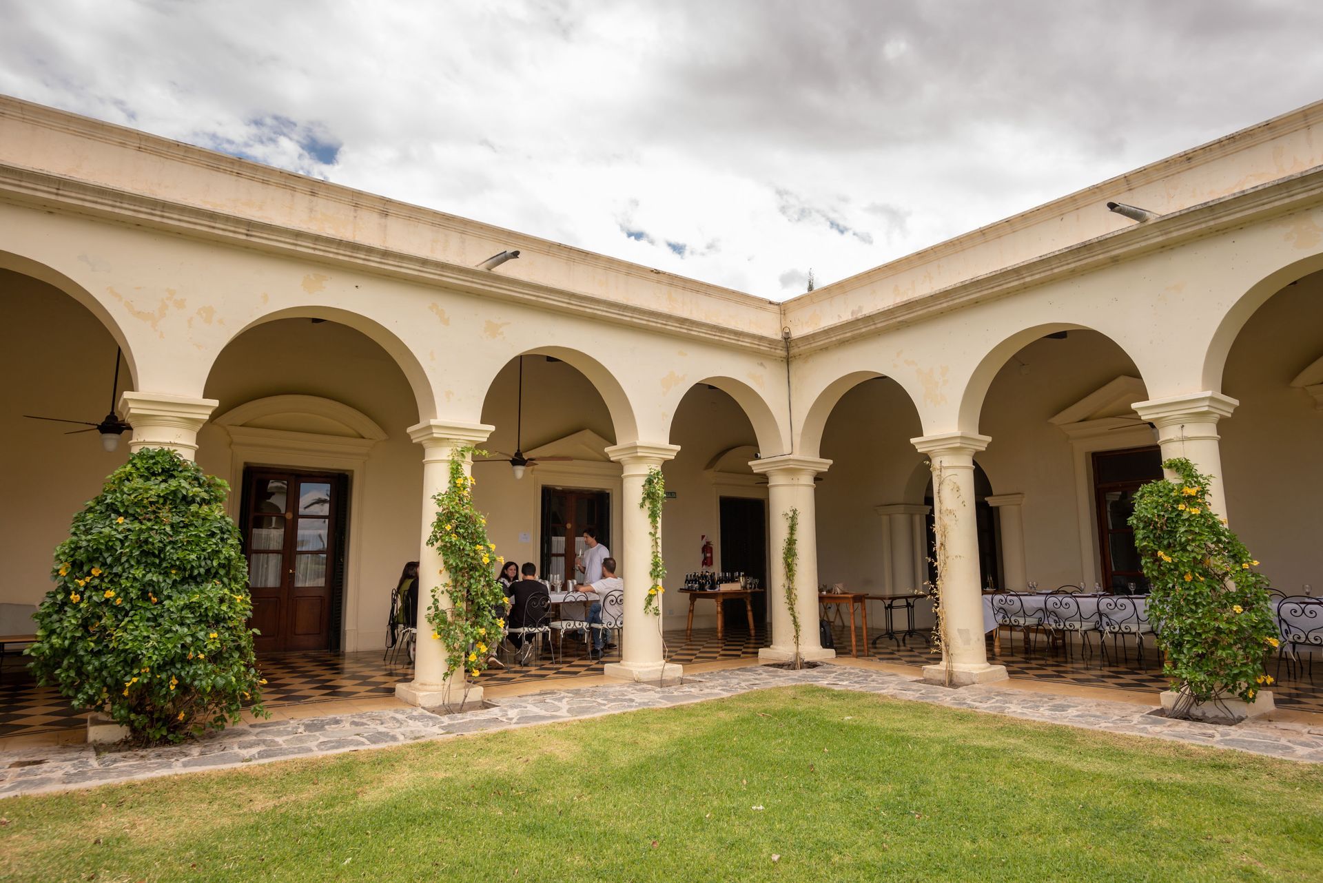 A courtyard with arches and columns and people sitting at tables.