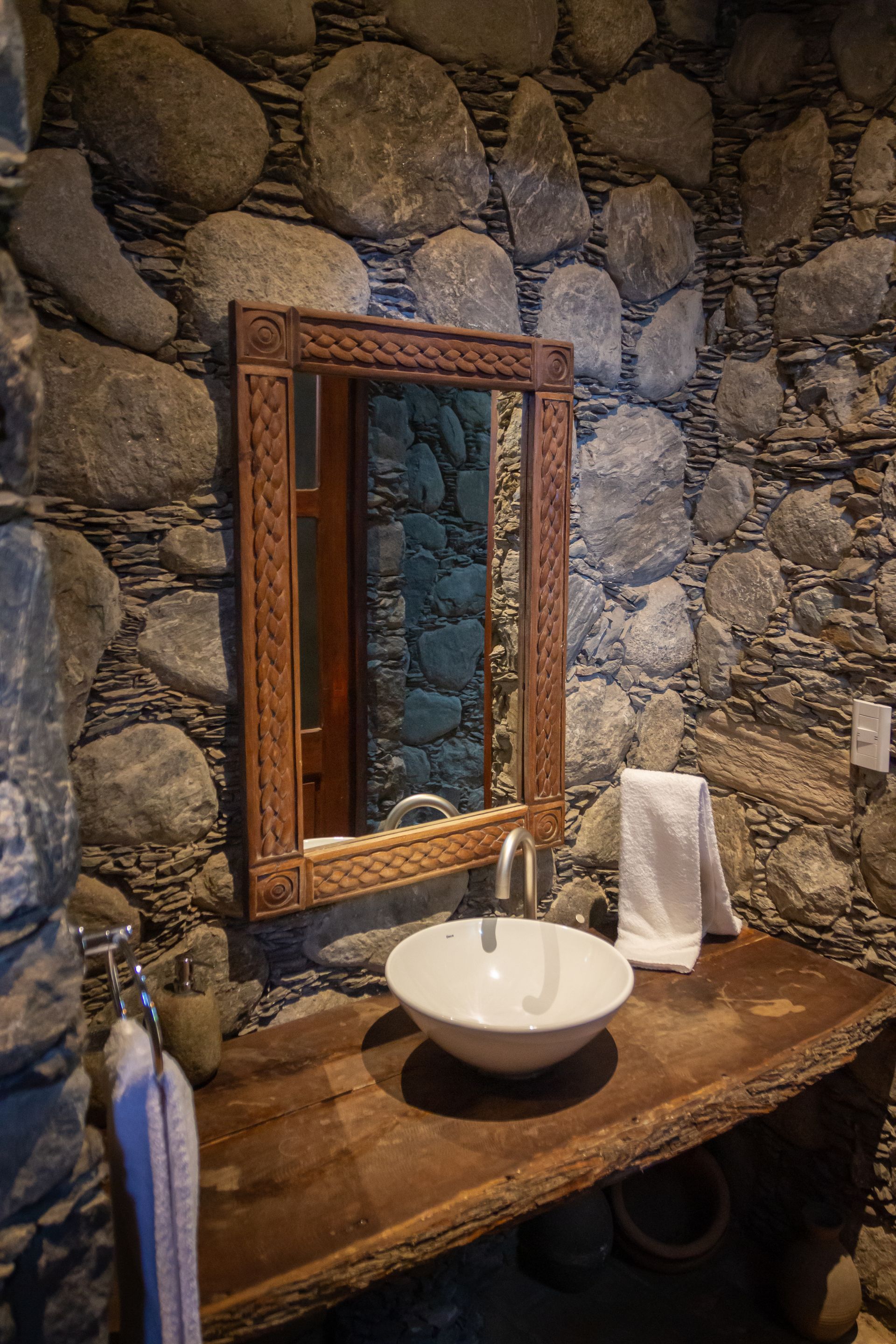 A bathroom with a sink , mirror and stone wall.