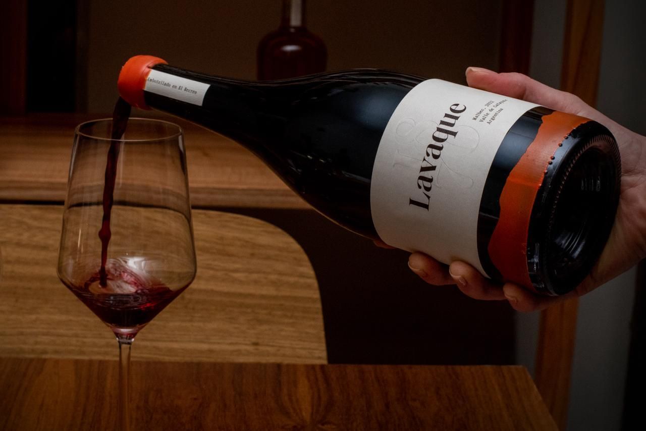 Red wine being poured from a bottle into a glass on a wooden surface.