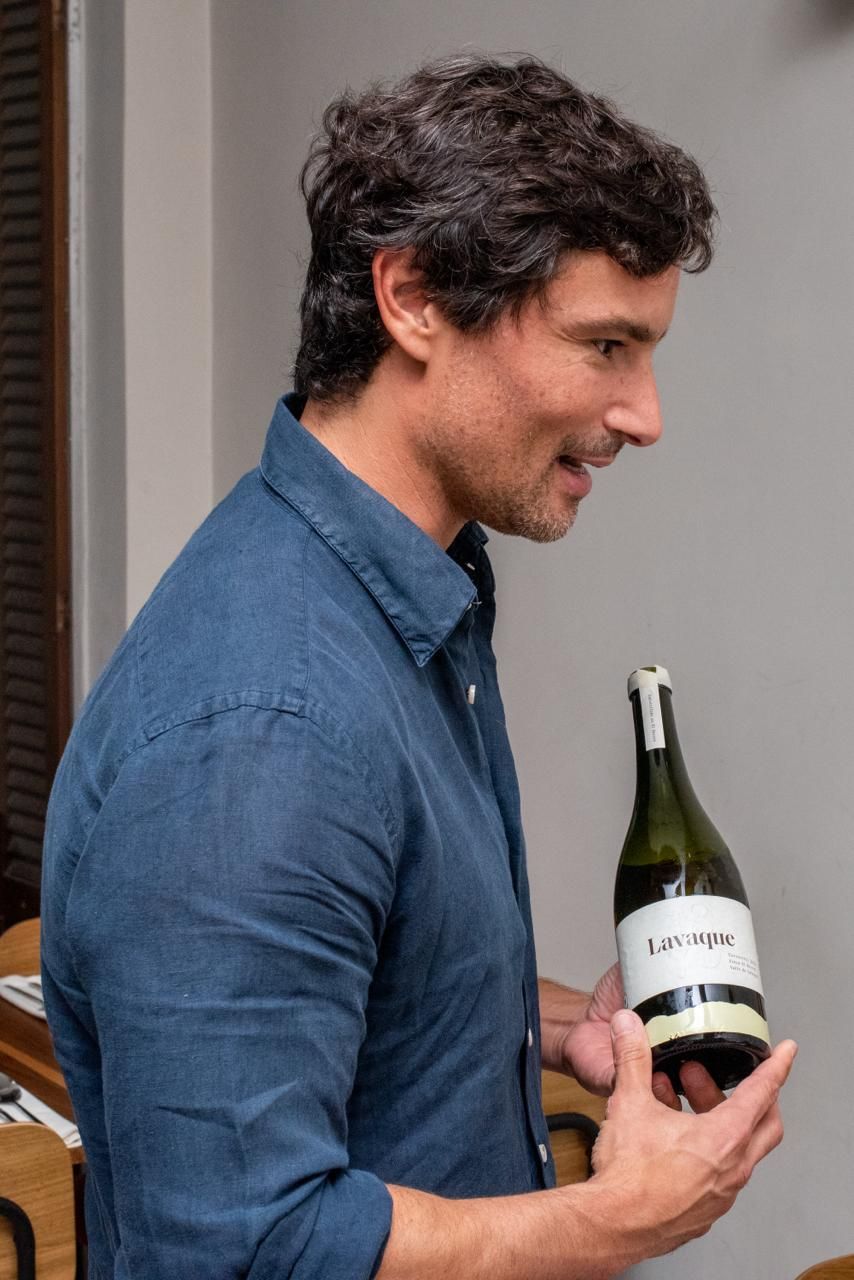 Man in blue shirt holding and looking at a wine bottle indoors.
