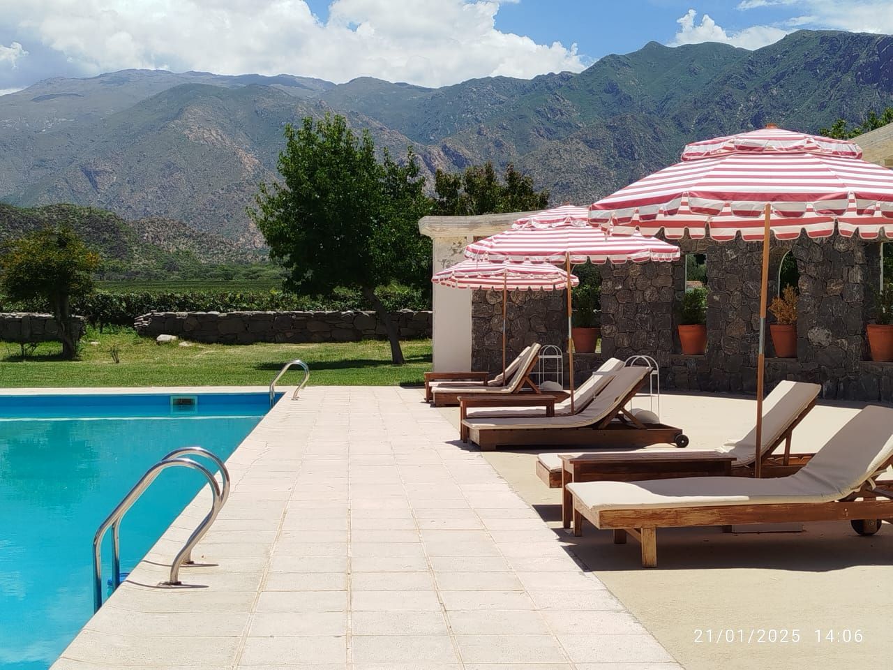 Swimming pool with lounge chairs and striped umbrellas against a mountain backdrop.