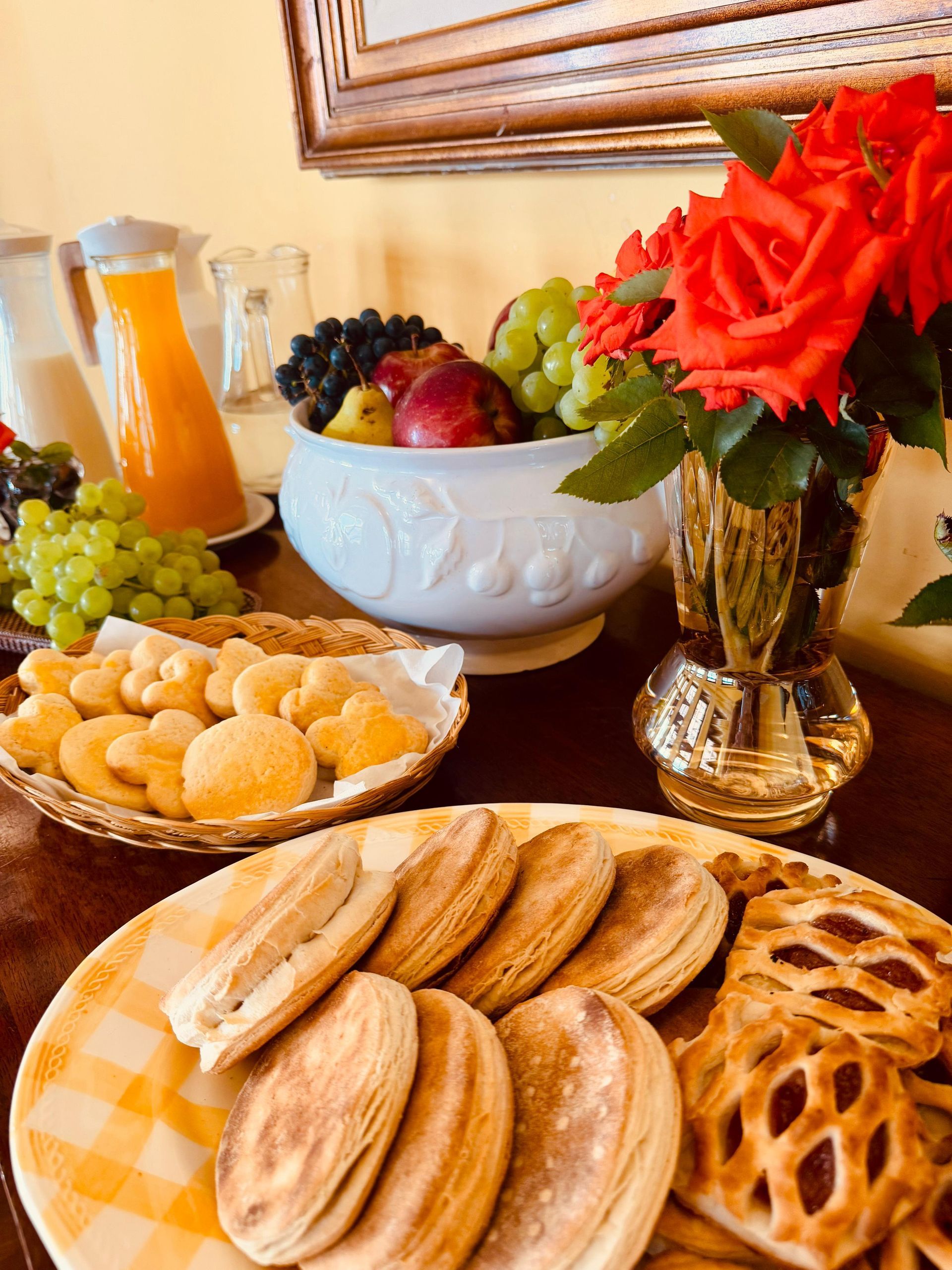 Breakfast spread with pastries, fruit, juice, and flowers on a table.