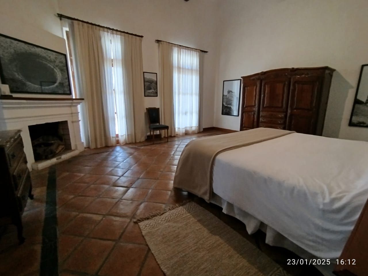 Bedroom with fireplace, bed, and antique wooden wardrobe; terracotta tile floor.