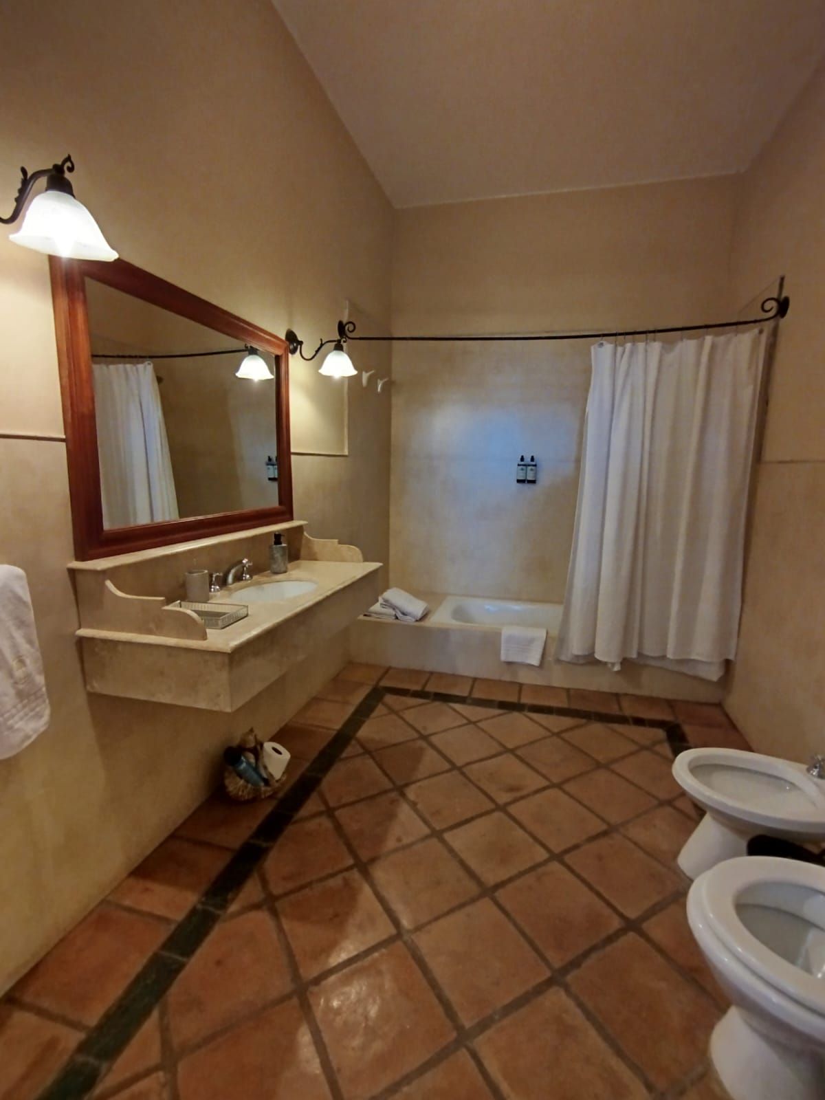 Bathroom with tiled floor, white fixtures, tub with shower curtain, and dark-framed mirror.