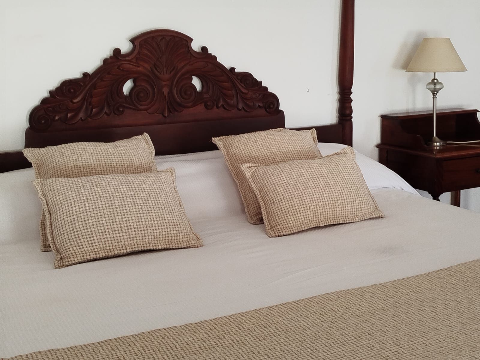 Bed with decorative wooden headboard and woven pillows. Nightstand with lamp beside bed.