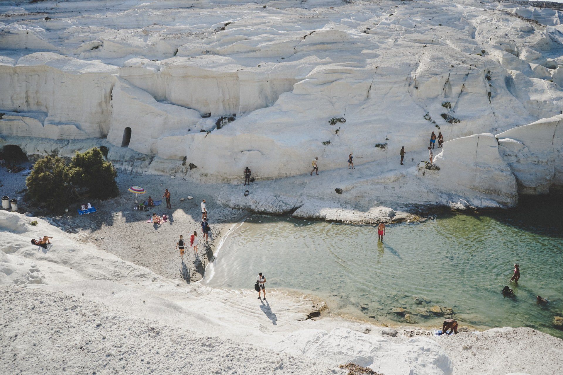 A group of people are standing on a beach next to a body of water.