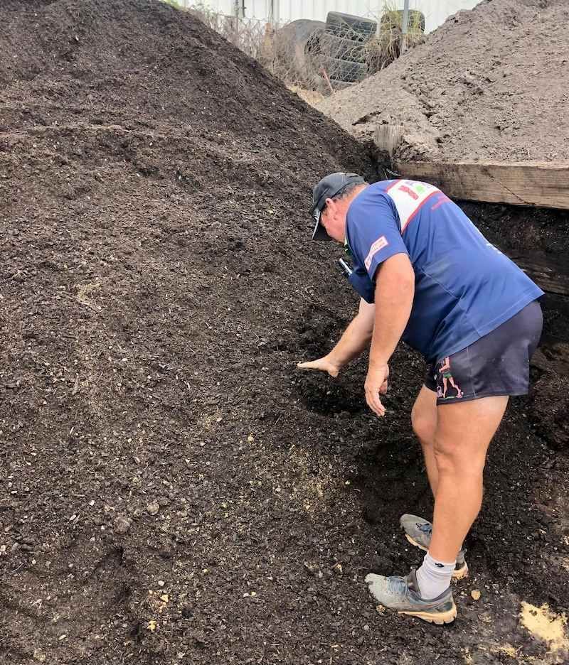 A Man is Standing in Front of a Pile of Dirt — Highfields Landscape Supplies In Toowoomba, QLD