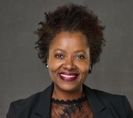 Smiling person with short curly hair in a black-and-white portrait