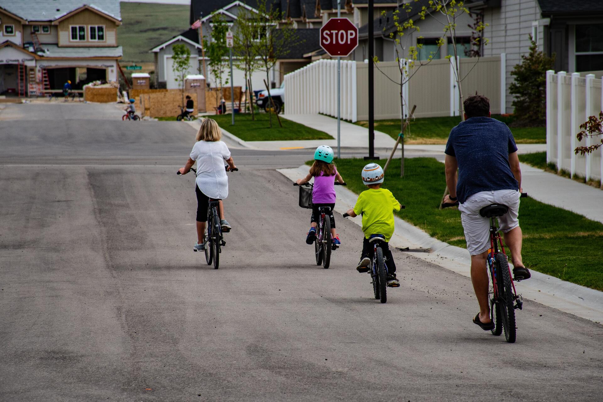 Four children ride bicycles down a suburban street toward a stop sign.