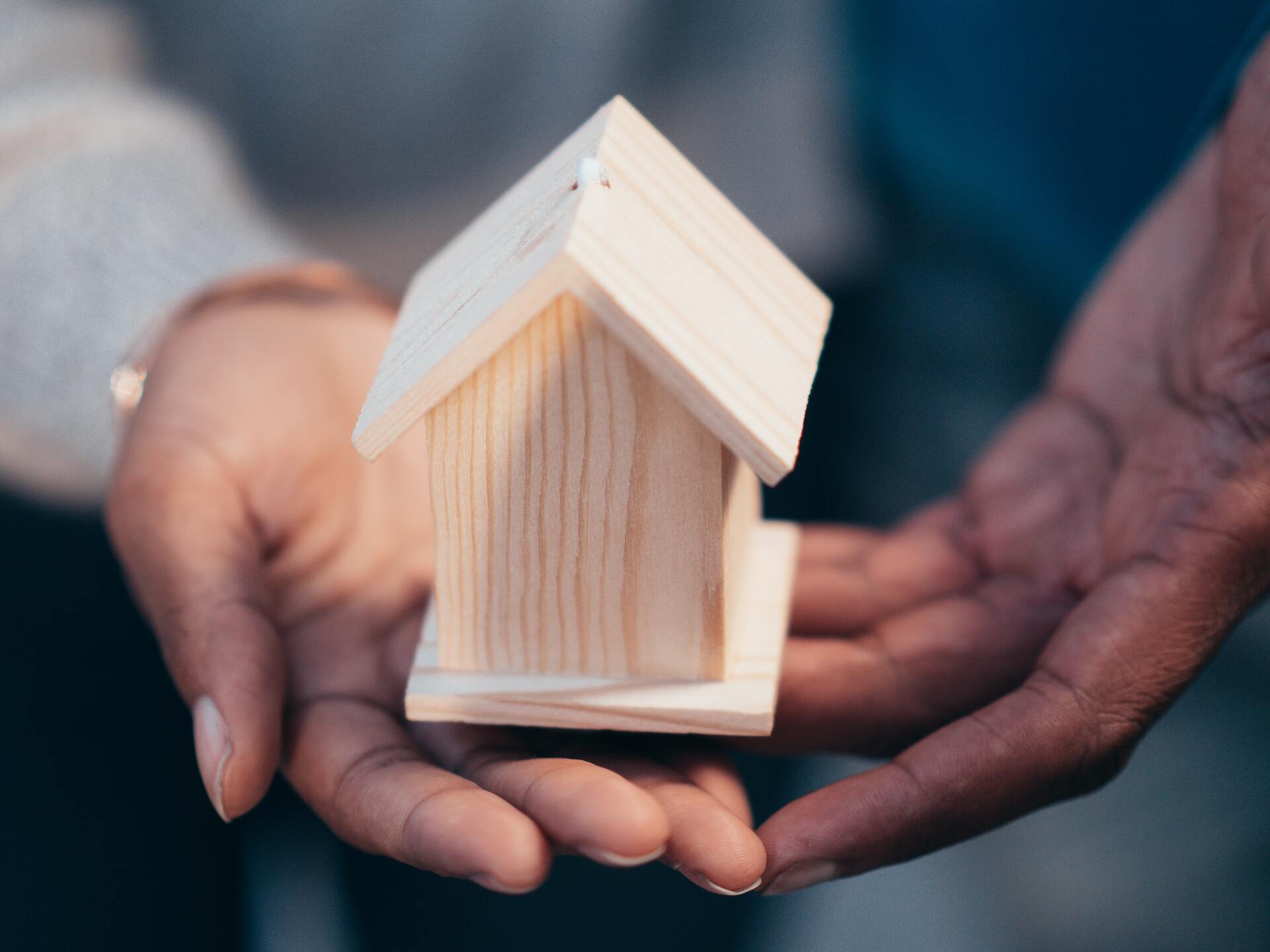 Hands gently holding a small wooden house model