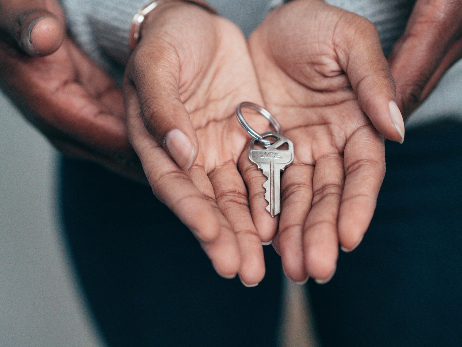 Hands holding a silver key on a keyring over a dark background