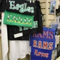Rack of school spirit shirts in black, green, and blue with Eagles and Rams text