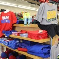 Clothing store display with folded red, blue, and gray graphic sweatshirts on shelves and hanging tops.