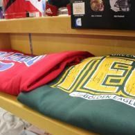 Two folded sweatshirts on a store shelf, one red and one green with a yellow “Eagle” logo.