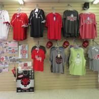 T-shirts displayed on a slatwall in a retail store, mostly red, black, gray, and neon green designs.
