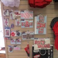 Clothing store display wall with red and black graphic T-shirts, accessories, and novelty items