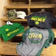 Assorted T-shirts and caps displayed on wooden shelves in a store, featuring green and gray designs.