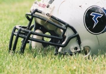Football helmet lying in grass, black facemask visible, with a blue logo on the side