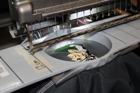 Embroidery machine stitching a design onto a green fabric hoop