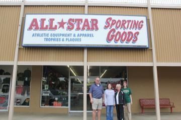 People standing outside All Star Sporting Goods storefront under red-and-blue sign