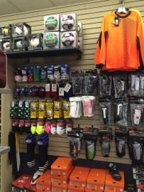 Sports store display with neon orange jersey, hanging socks, gloves, and stacked orange shoe boxes