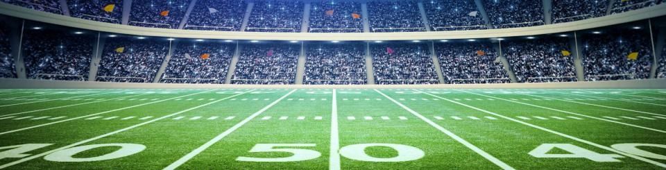 Empty football stadium with green field and white yard lines, including the 50-yard line at center