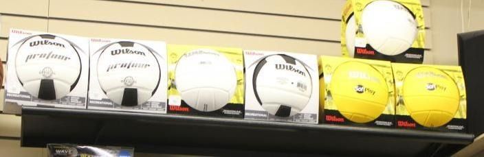 White and yellow soccer balls displayed on a shelf with labels beneath them.
