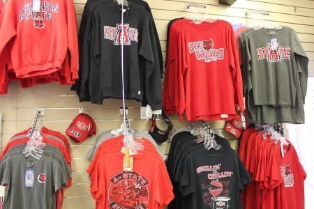 Clothing store display of red, black, and olive graphic sweatshirts and caps on a wall rack