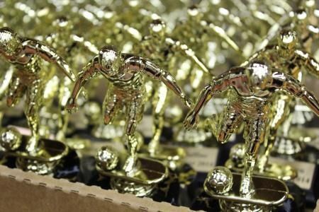 Rows of gold trophies with figurines, displayed on a table in a store.