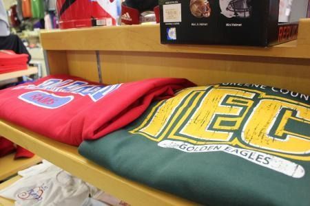 Folded red and green sweatshirts on a store display shelf, with a yellow graphic logo.