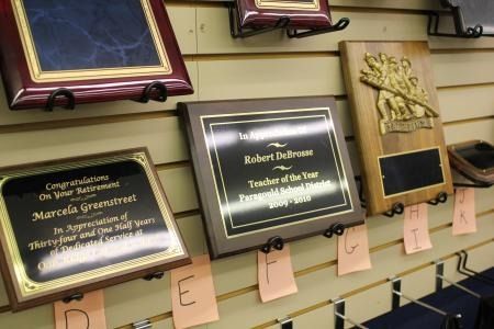 Display of engraved plaques and awards on a shelf with hanging tags beneath them