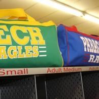 Green and blue sports bags hanging on display above locker shelves