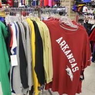 Racks of colorful shirts in a store, including a red Arkansas T-shirt in front
