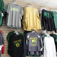 Racks of high school logo T-shirts in green, gray, yellow, and black displayed in a shop