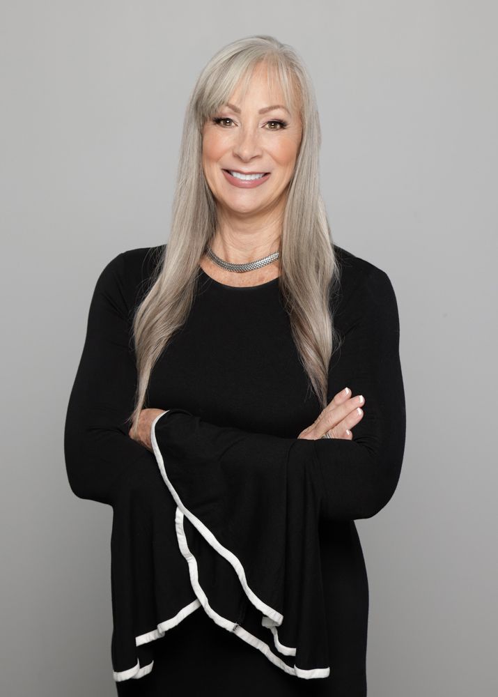 A woman in a black sweater is standing with her arms crossed and smiling.