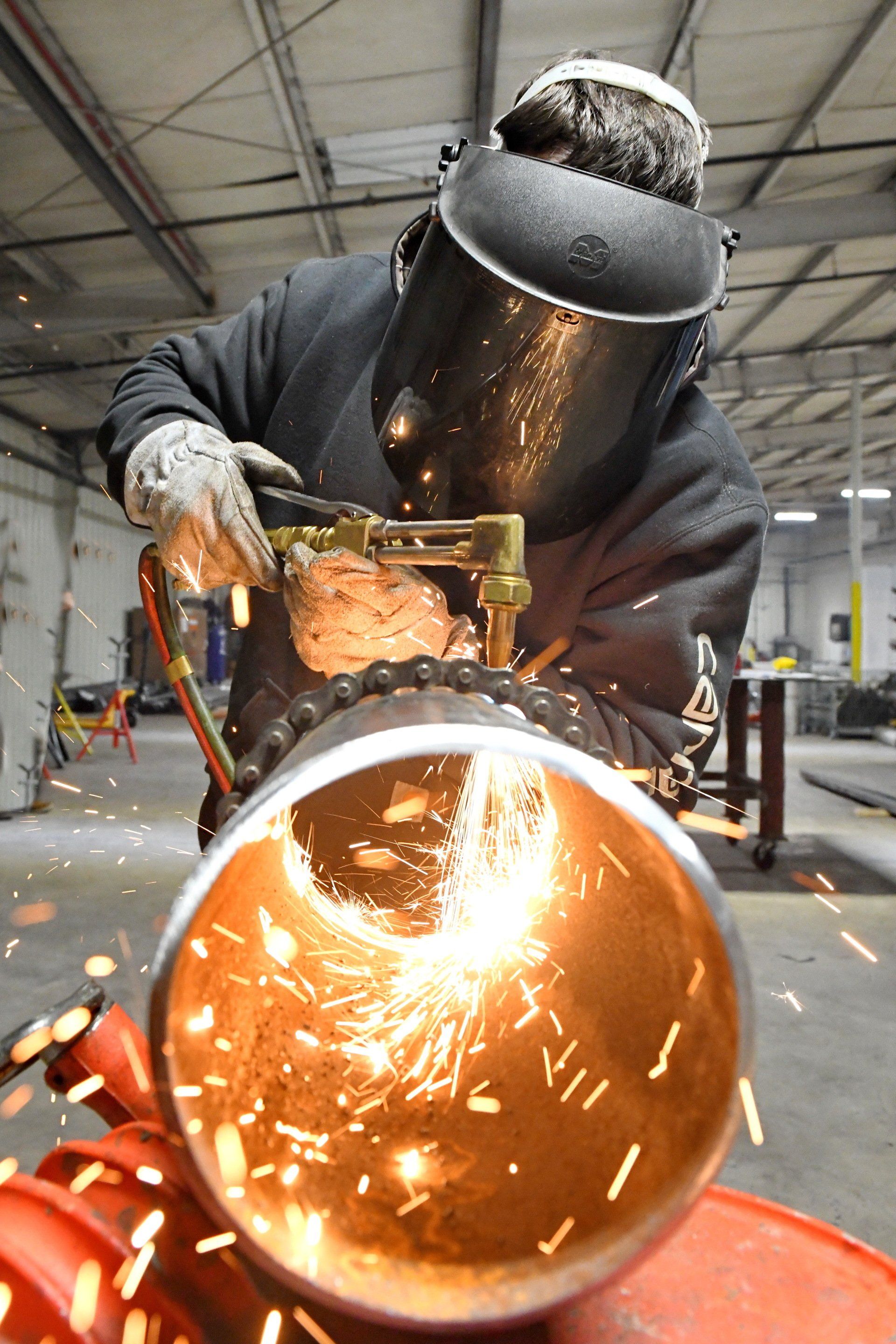 A man wearing a welding mask is welding a pipe in a factory