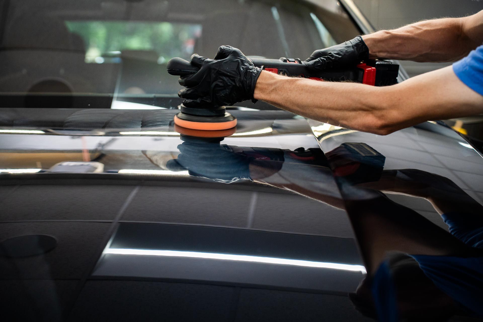 A man is polishing the hood of a car with a machine.