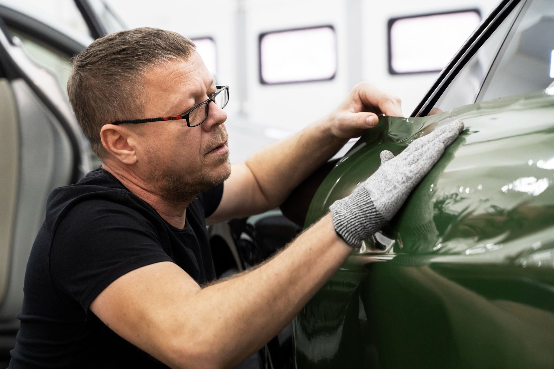 A man is working on a green car in a garage.