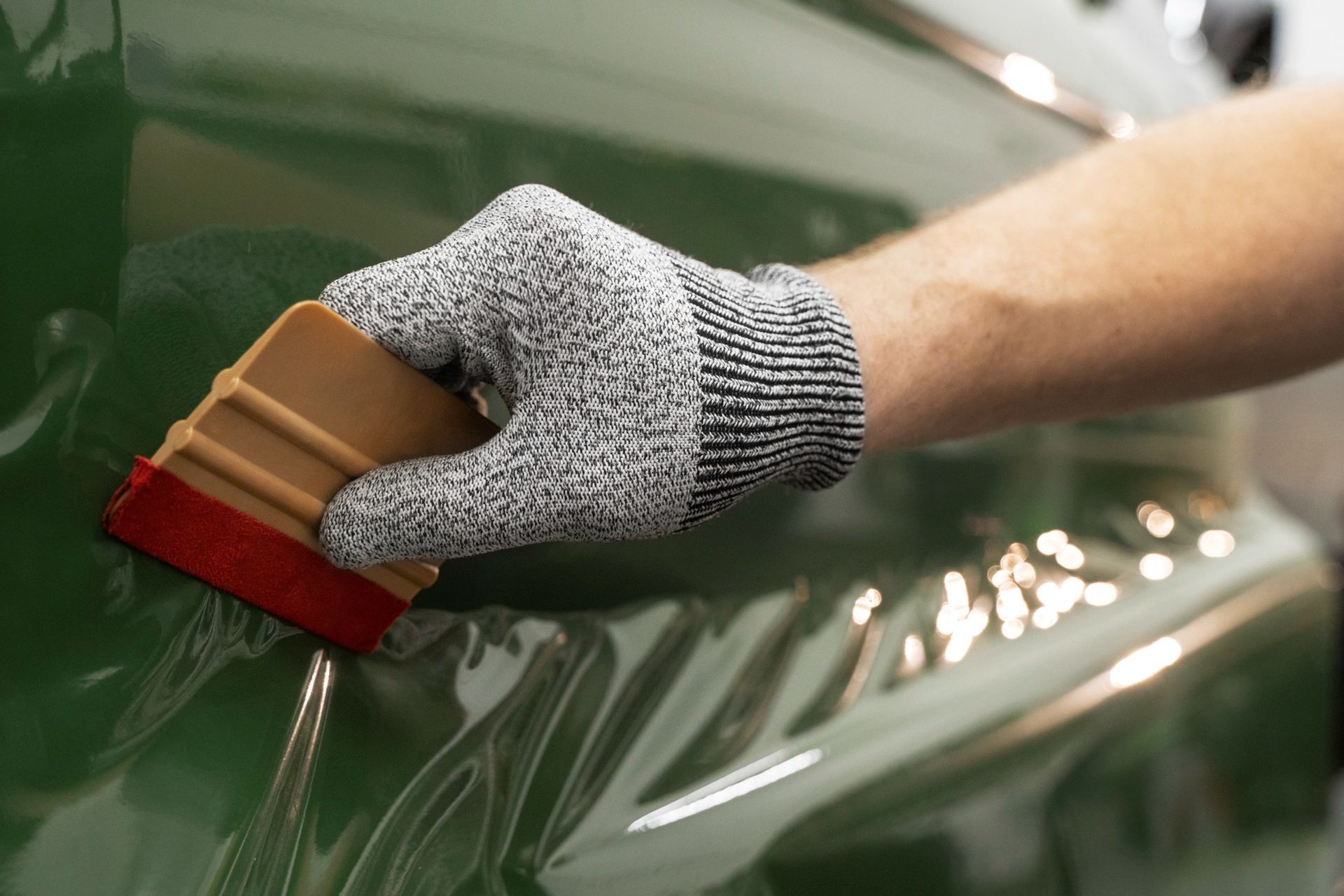 A person wearing a glove is using a squeegee on a green car.