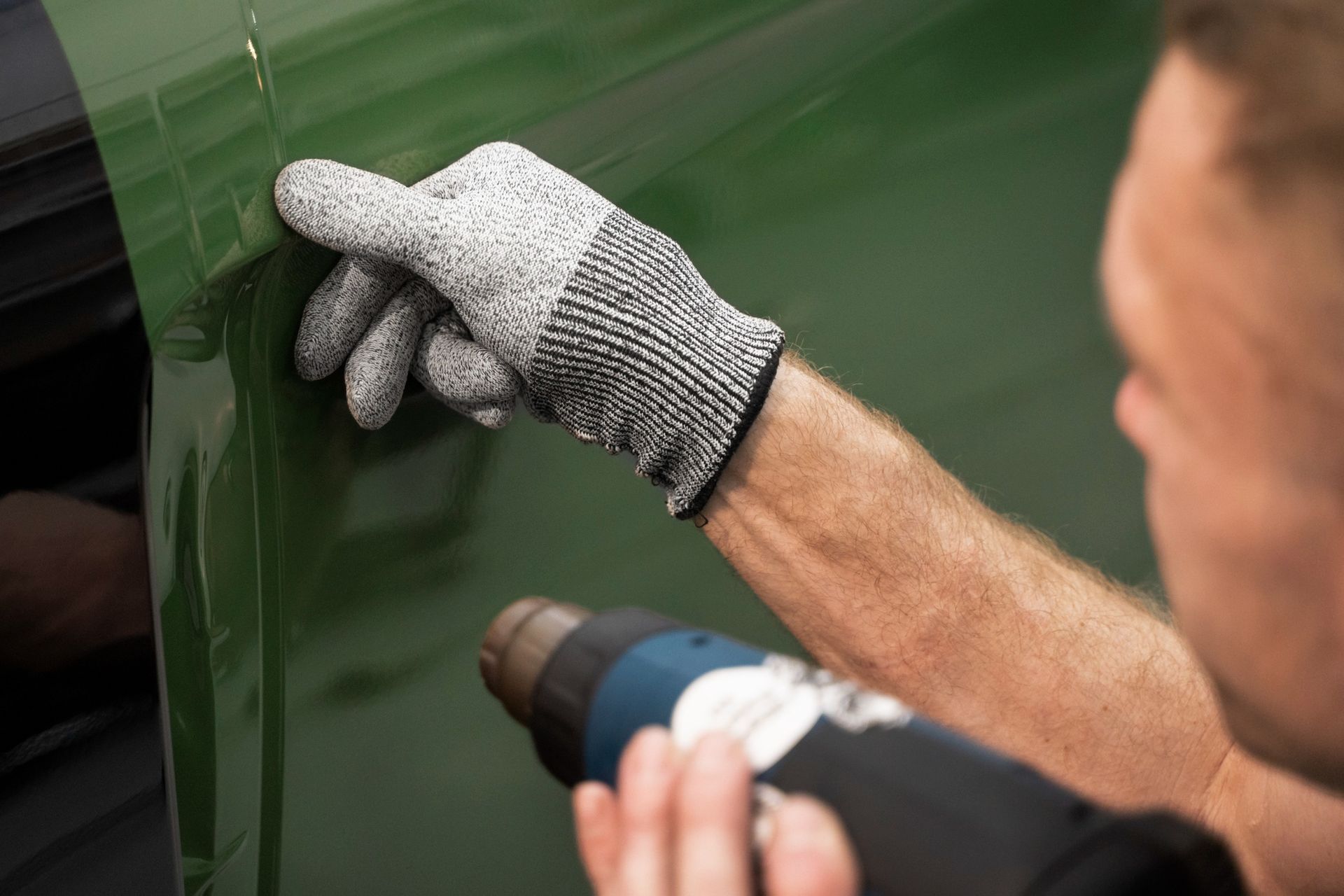 A person is polishing a blue car with a cloth.