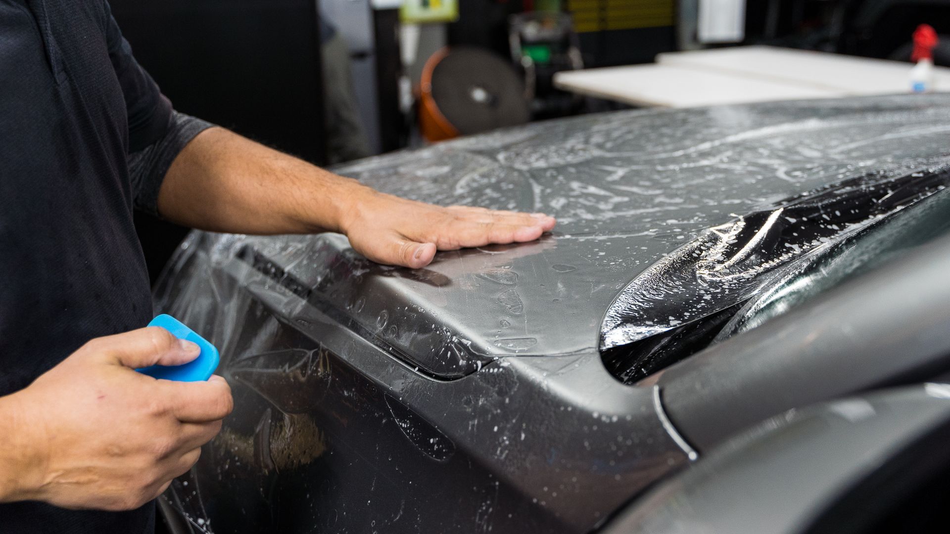 A man is applying a protective film to the hood of a car.