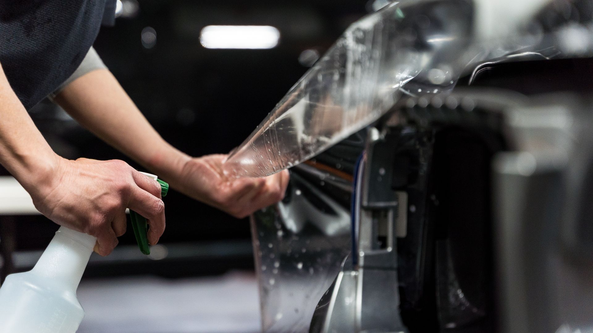 A man is applying a protective film to the side of a car.