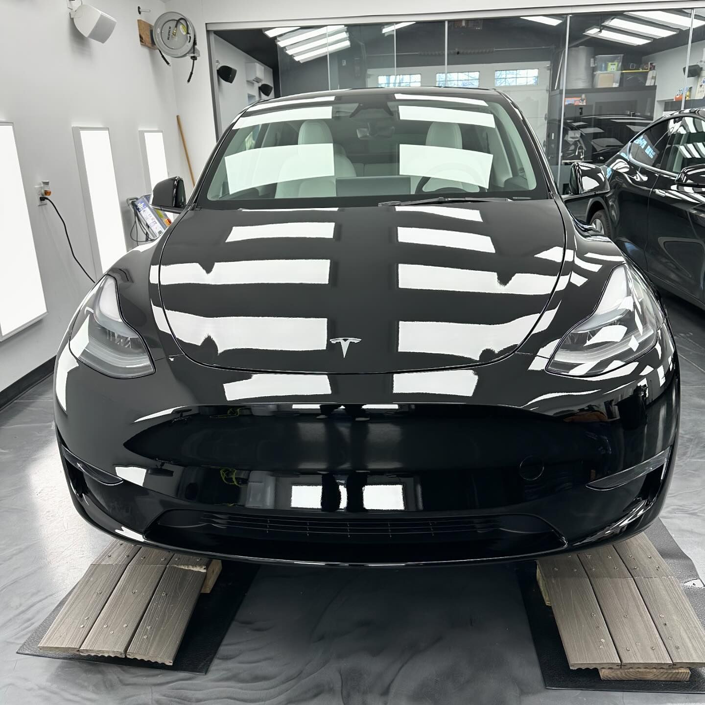 A black tesla model 3 is sitting on wooden ramps in a garage.