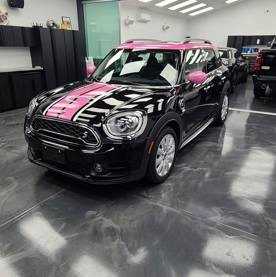 A black car with a pink stripe on the side is parked in a garage